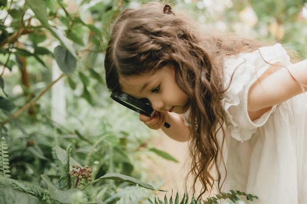 Portrait d'une jolie petite fille regardant les plantes à travers une loupe Un enfant avec une loupe étudie la nature dans le jardin Le concept de développement précoce