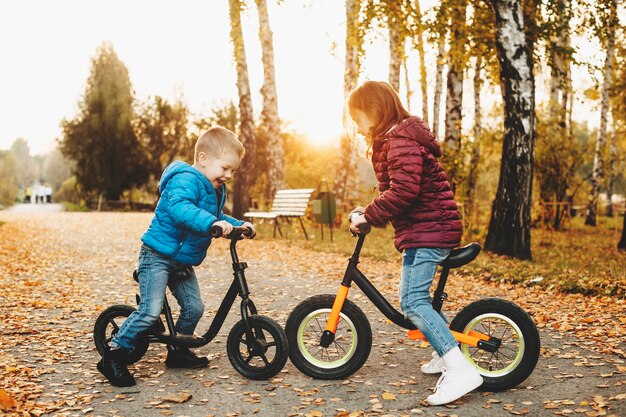 Portrait d'une jolie petite fille et son frère jouant avec leurs vélos face à face dans le parc.