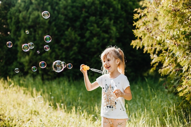 Portrait d'une jolie petite fille soufflant des bulles de savon dans le parc en été