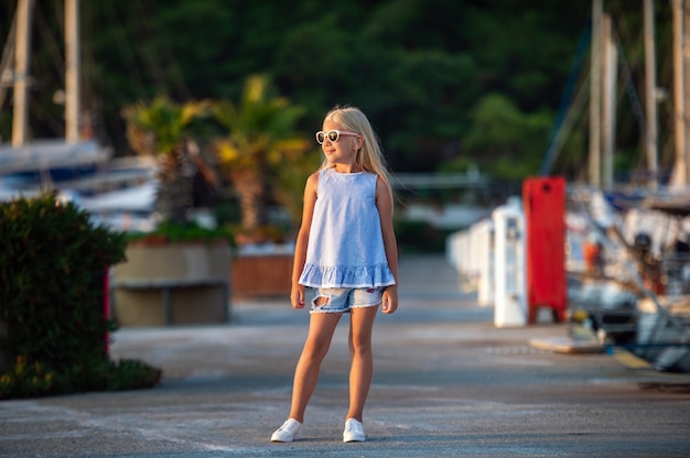 Portrait d'une jolie petite fille souriante avec des lunettes.Une fille en short et un T-shirt bleu au coucher du soleil au bord de la mer.Turquie
