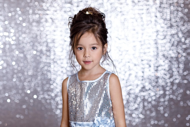 Portrait d'une jolie petite fille souriante en robe argentée et bleue sur fond avec bokeh argenté. fête d'anniversaire