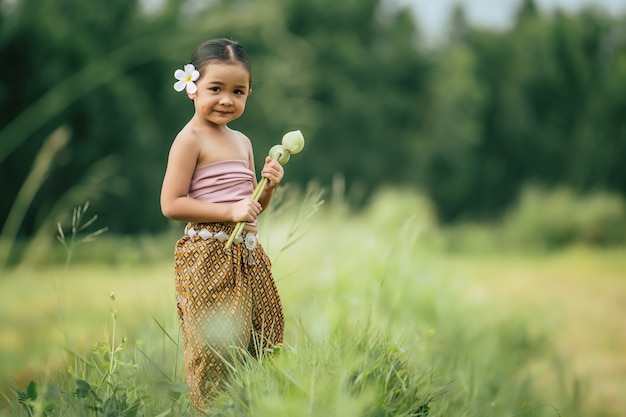 Portrait de jolies filles en costume traditionnel thaïlandais et mettant une fleur blanche sur son oreille, debout et tenant deux lotus à la main sur une rizière, elle sourit de bonheur, espace pour copie