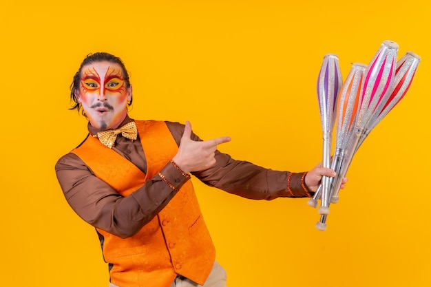 Portrait d'un jongleur heureux en gilet de maquillage jonglant avec des masses sur fond jaune