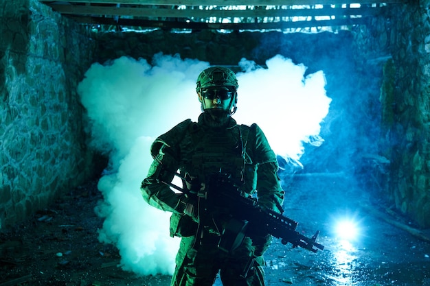 Portrait d'un joueur d'airsoft dans un équipement professionnel avec une mitrailleuse dans un bâtiment en ruine abandonné. Soldat avec des armes en guerre dans la fumée et le brouillard