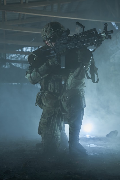Portrait d'un joueur d'airsoft dans un équipement professionnel avec une mitrailleuse dans un bâtiment en ruine abandonné. Soldat avec des armes en guerre