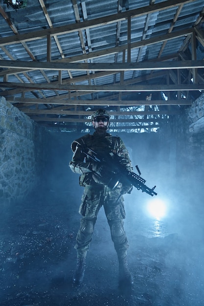 Portrait d'un joueur d'airsoft dans un équipement professionnel avec une mitrailleuse dans un bâtiment en ruine abandonné. Soldat avec des armes en guerre