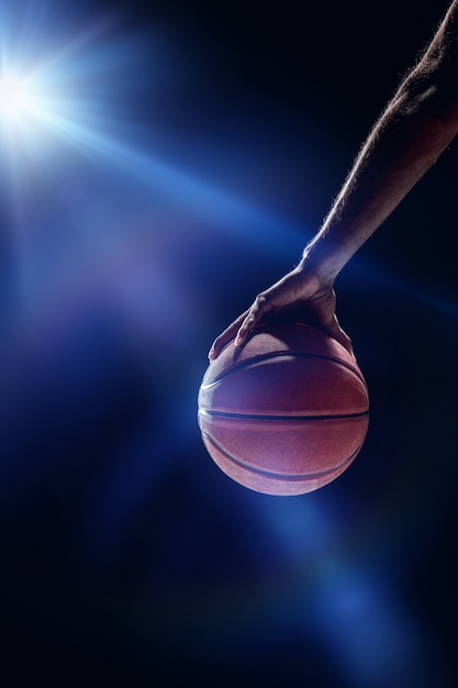 Le portrait d'un joueur de basket-ball avec un ballon sur fond de studio sombre. concept publicitaire