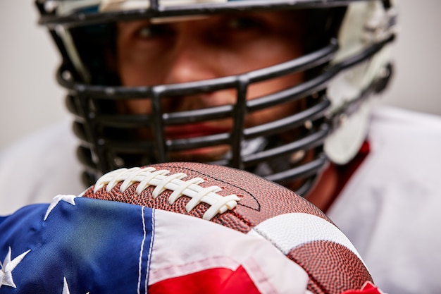 Portrait de joueur de football américain en casque avec ballon et drapeau américain fier de son pays