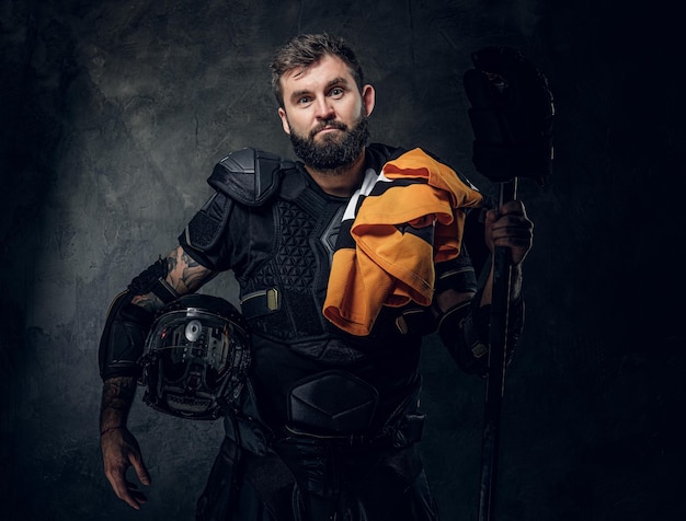 Portrait d'un joueur de hockey barbu sérieux avec son équipement de sport dans les mains.