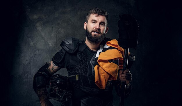 Portrait d'un joueur de hockey barbu sérieux avec son équipement de sport dans les mains.