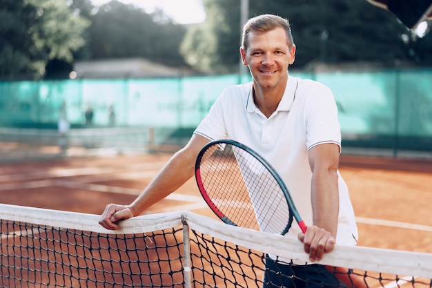 Portrait de joueur de tennis masculin positif avec raquette debout à terre battue