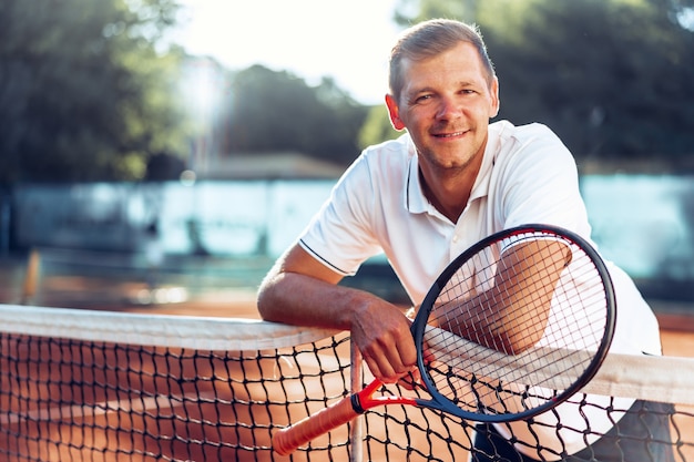 Portrait de joueur de tennis masculin positif avec raquette debout à terre battue