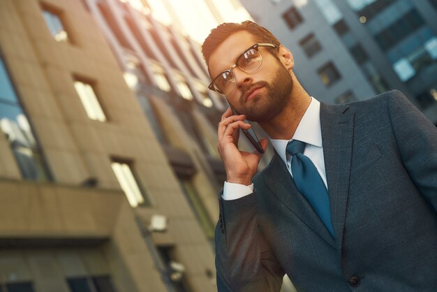 Portrait d'une journée bien remplie d'un bel homme barbu en costume parlant par téléphone avec le client tout en