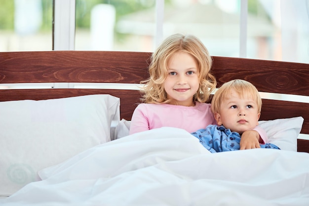 Portrait de jours paresseux de cure petite soeur et frère en pyjama regardant la caméra et