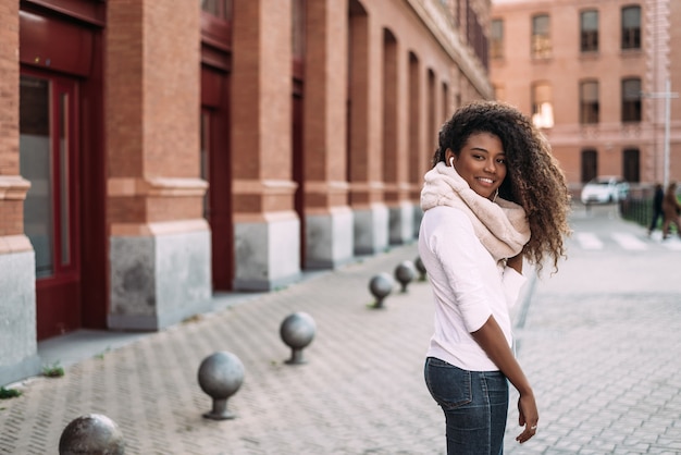 Portrait de joyeuse demoiselle dehors dans la rue en écoutant de la musique avec des écouteurs.