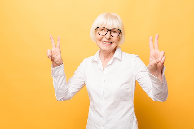 Portrait d'une joyeuse femme senior gestes victoire isolée sur fond jaune.