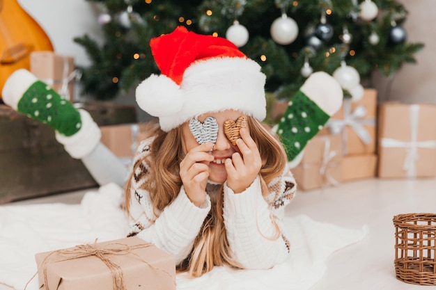 Portrait d'une joyeuse fille de 8 ans allongée sur le sol près de boîtes avec des cadeaux et un arbre de Noël à la maison.