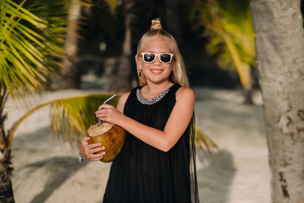 Portrait d'une joyeuse fille de 9 ans avec un cocktail de noix de coco sur fond de palmiers sur une plage exotique petite fille avec une noix de coco sur la plage de l'île Maurice
