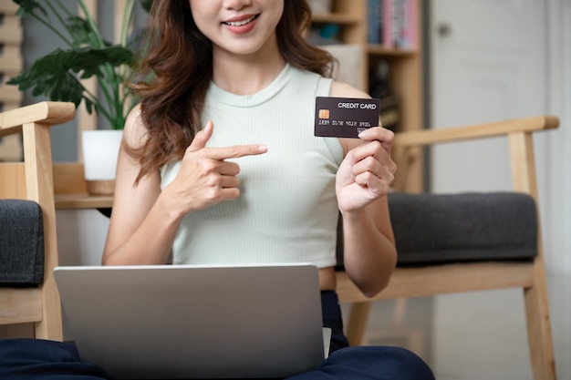 Portrait joyeuse fille d'Asie shopping en ligne et tenant dans les mains démontrant la carte bancaire à la maison