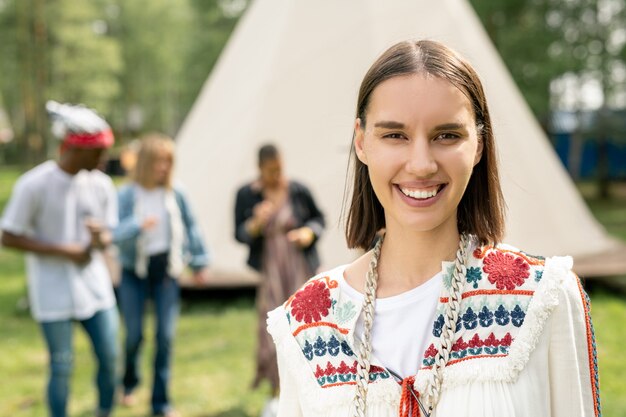 Portrait de joyeuse fille brune hippie debout contre la tente de camping et les gens qui dansent