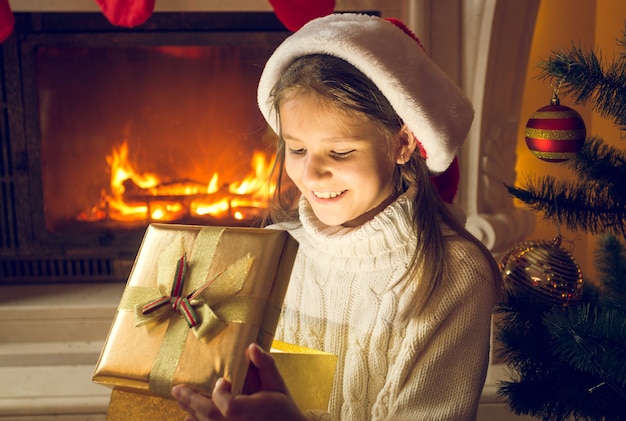 Portrait de joyeuse fille souriante assise près de la cheminée et regardant à l'intérieur de la boîte actuelle