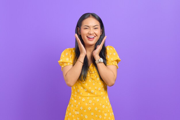 Portrait de joyeuse jeune femme asiatique debout avec les bras levés sur fond violet