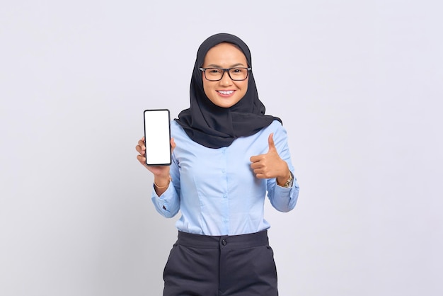 Portrait de joyeuse jeune femme asiatique montrant un téléphone portable à écran blanc et gesticulant les pouces vers le haut isolé sur fond blanc