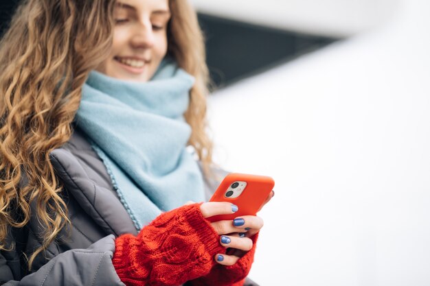 Portrait de joyeuse jeune femme aux cheveux bouclés textos sur smartphone debout sur la rue dans la ville d'hiver le nouvel an.