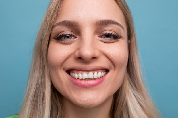 Portrait d'une joyeuse jeune femme blonde en bonne santé avec un sourire hollywoodien sur fond bleu