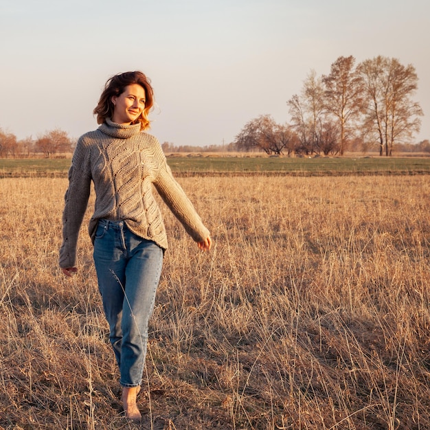 Portrait joyeuse jeune femme brune en pull en tricot marron en laine naturelle et jeans s'amusant sourire et profiter de la journée sur le terrain femme hipster élégante Photo de style de vie atmosphérique en plein air