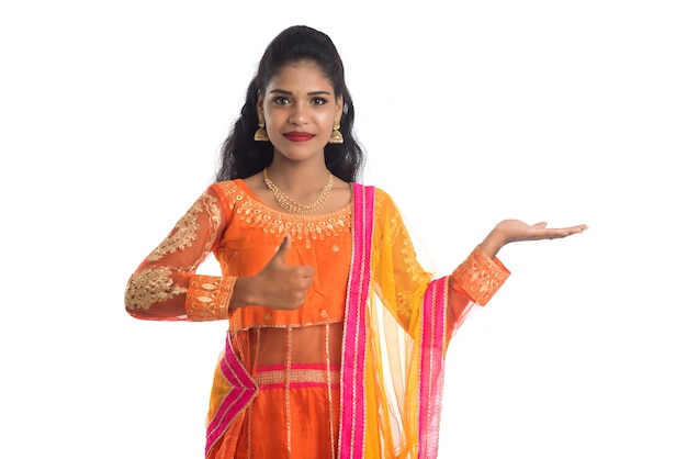 Portrait de joyeuse jeune femme traditionnelle indienne présentant quelque chose sur place, montrant l'espace de copie sur sa paume sur un mur blanc