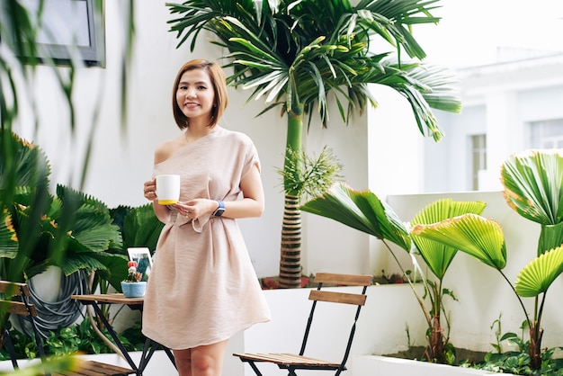 Portrait de joyeuse jeune femme vietnamienne posant avec une tasse de délicieux café chaud à table de café