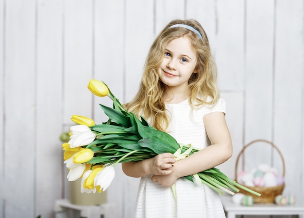 Portrait de joyeuse petite fille blonde avec bouquet de tulipes sur fond de bois blanc.