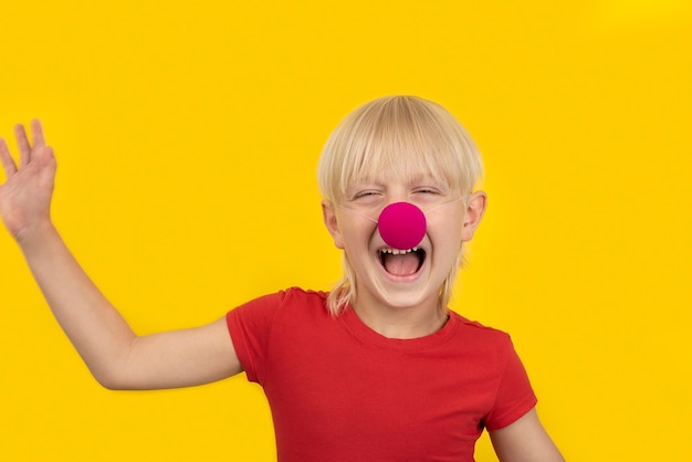 Portrait de joyeux garçon blond avec nez de clown sur une surface jaune