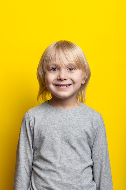 Portrait de joyeux garçon fairhaired aux cheveux longs sur fond jaune vif Cadre vertical