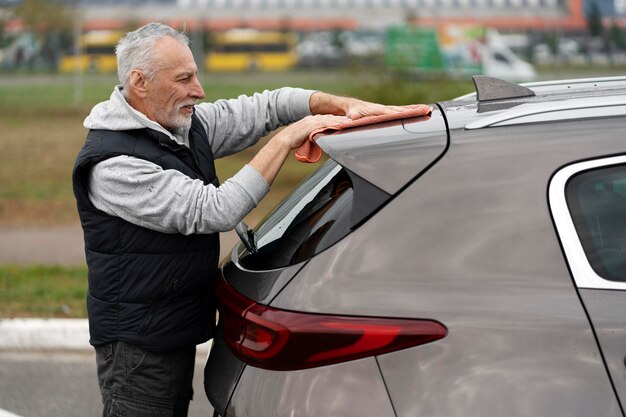 Portrait latéral bel homme âgé en vêtements décontractés nettoyant la voiture dans la station de lavage de voiture en libre-service