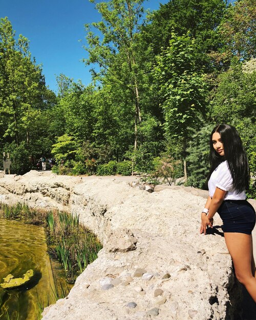 Photo portrait latéral d'une jeune femme debout contre des arbres par une journée ensoleillée