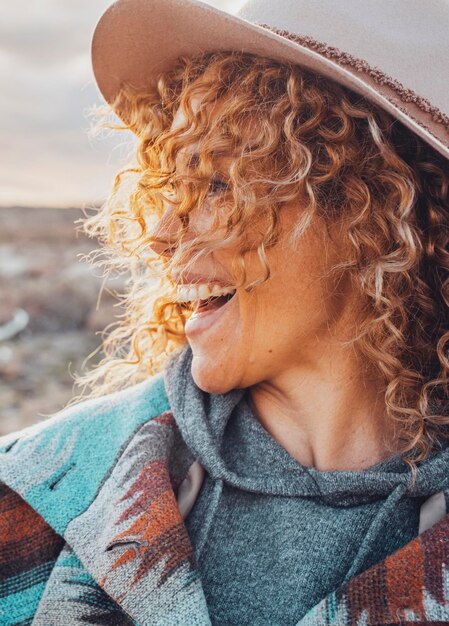 Portrait latéral d'une jolie femme joyeuse et excitée avec des cheveux blonds bouclés et un chapeau s'amuser dans les activités de loisirs de voyage en plein air Les femmes touristiques sourient et rient beaucoup à la campagne