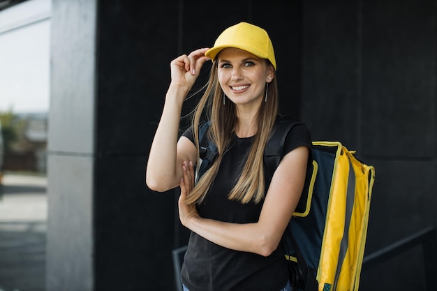 Portrait de livraison de nourriture d'une femme caucasienne de messagerie avec sac à dos jaune et casquette
