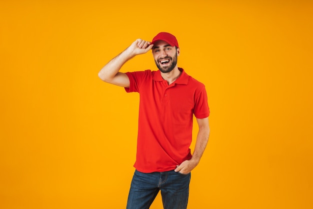 Portrait d'un livreur heureux en t-shirt rouge et casquette souriant et se présentant à la caméra isolée sur jaune