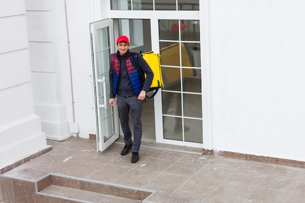 Portrait d'un livreur joyeux debout avec un sac à dos thermo jaune pour la livraison de nourriture dans la rue à l'extérieur