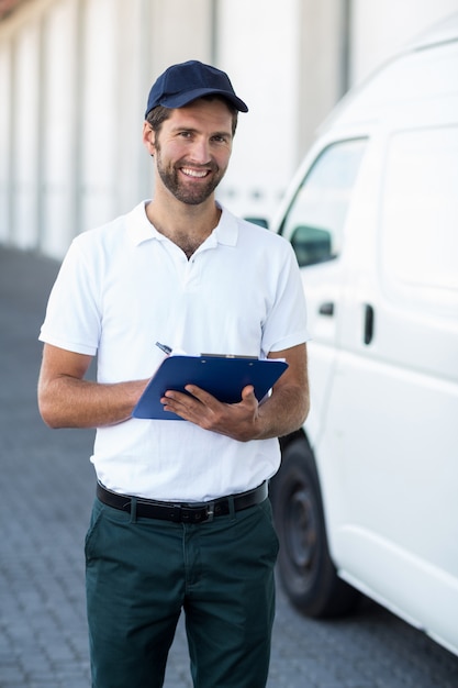 Portrait de livreur tenant un presse-papiers à côté de sa camionnette