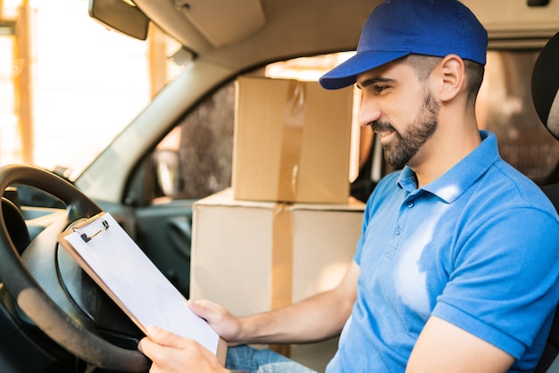 Portrait d'un livreur vérifiant la liste de livraison alors qu'il était assis dans une camionnette. Concept de livraison et d'expédition.