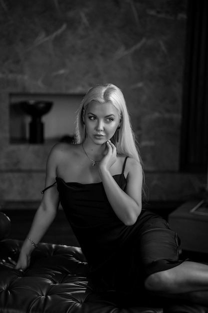 Portrait d'une luxueuse jeune femme blonde vêtue d'une robe sexy noire Dans un intérieur sombre