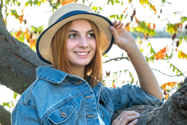 Photo portrait d'une magnifique adolescente souriante au chapeau jaune et aux cheveux rouges portant une veste en jean à l'extérieur