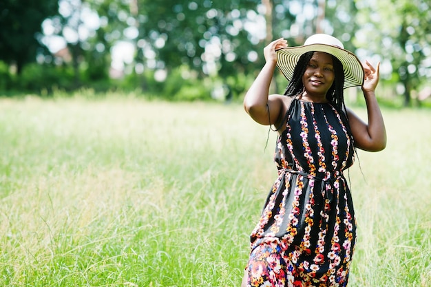 Portrait d'une magnifique femme afro-américaine des années 20 en chapeau d'été posant sur l'herbe verte dans le parc.