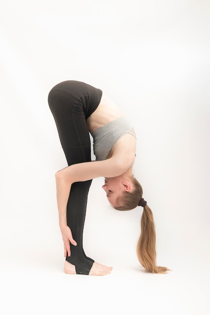 Portrait d'une magnifique jeune femme pratiquant le yoga. Fille flexible se pencha à ses pieds. Gymnastique sur fond blanc. Yoga et Pilates. Châssis vertical