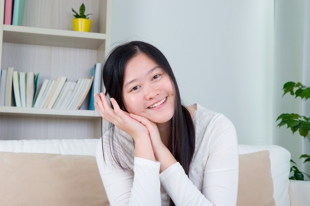 Portrait de main de fille asiatique tenant visage, détendu et souriant à la maison, fille adulte vivant à l&#39;intérieur de style de vie.