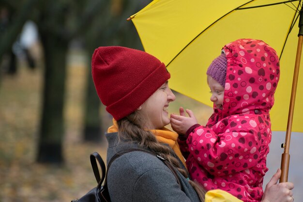 Photo portrait de maman et bébé sous parapluie jaune dans le parc. maman sourit à sa fille.