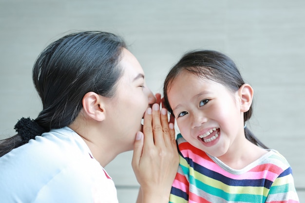 Portrait De Maman Heureuse Chuchotant Un Secret à L'oreille De Sa Petite Fille.